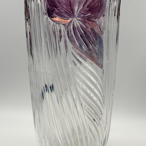 Könnte beinhalten: Transparente Glasvase mit einem lila Blumendesign. Die Vase hat eine hohe, zylindrische Form mit vertikalen, strukturierten Linien. Das Blumendesign ist durch das Glas sichtbar und verleiht der Vase ein dekoratives Element.
