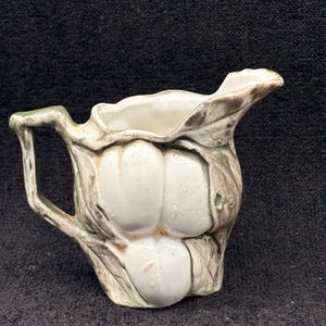 Puede incluir: Una taza de cerámica blanca con asa negra y el texto "But First, Coffee" en negrita negra. La taza se encuentra sobre un fondo borroso, sugiriendo un ambiente acogedor.