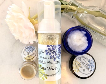 May include: Three small jars of skincare products with labels that say "Coffee Eye Cream", "Gentle Foaming Face Wash", and "Sugar Facial Scrub". The jars are on a white marble surface with a white rose and a glass vase.