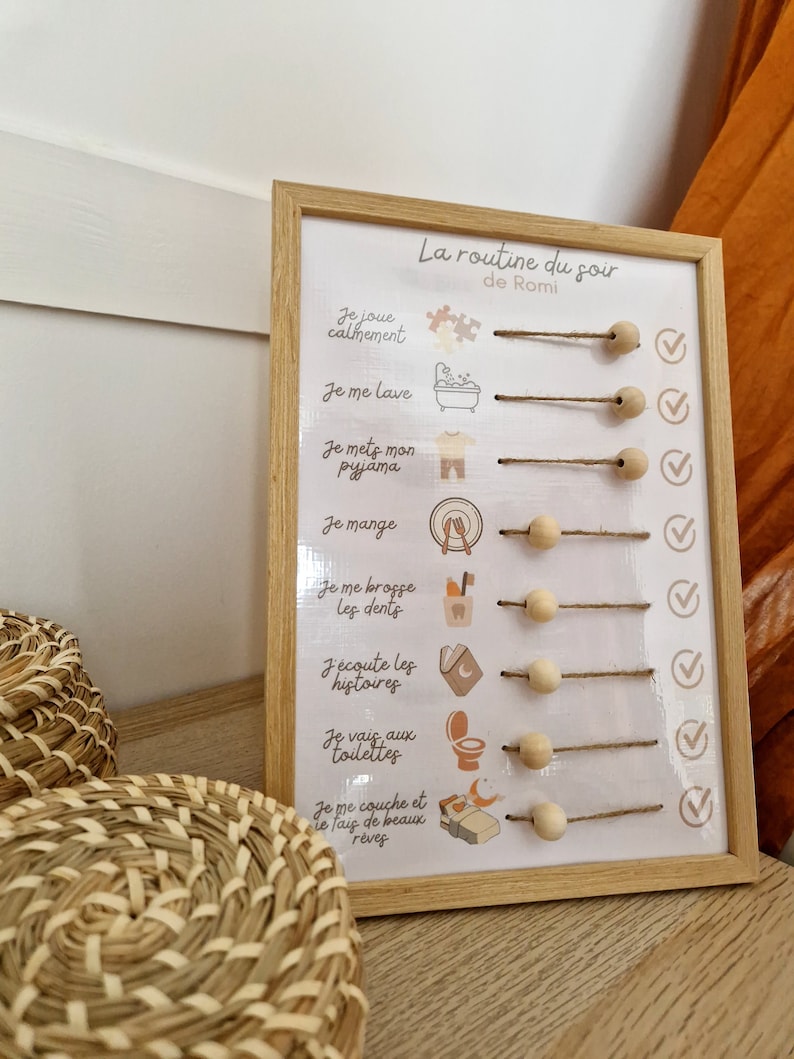 May include: A framed wooden chart with the text "La routine du soir de Romi" and illustrated steps for a bedtime routine. The steps include playing, washing, putting on pajamas, eating, brushing teeth, listening to stories, using the toilet, and going to bed.