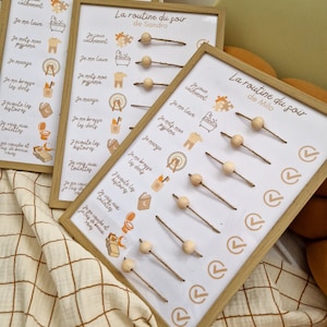 May include: Three framed chore charts with the text "La routine du soir" and names. Each chart has illustrations and text in French, with wooden beads on strings to track tasks. The frames are light wood.