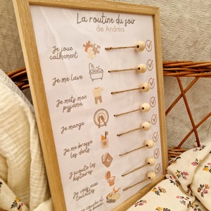 May include: A wooden framed chart with the text "La routine du soir de Andr&eacute;a" and illustrated steps for a bedtime routine. The chart includes text and icons for activities like playing, bathing, and brushing teeth. Wooden beads are attached to the chart.