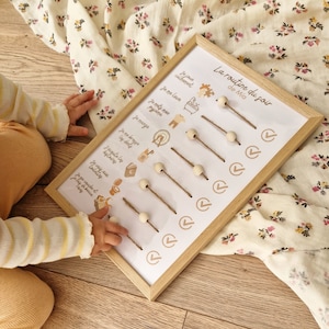 May include: A wooden framed chart with the text "La routine du soir de Mia" and illustrated steps for a bedtime routine. The chart includes wooden beads on strings and check marks. The background is a floral patterned fabric.