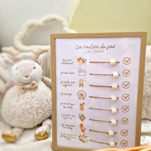 May include: A framed bedtime routine chart with the text "La routine du soir de Gabin". The chart includes illustrations and check boxes for each activity. A stuffed animal is in the background.