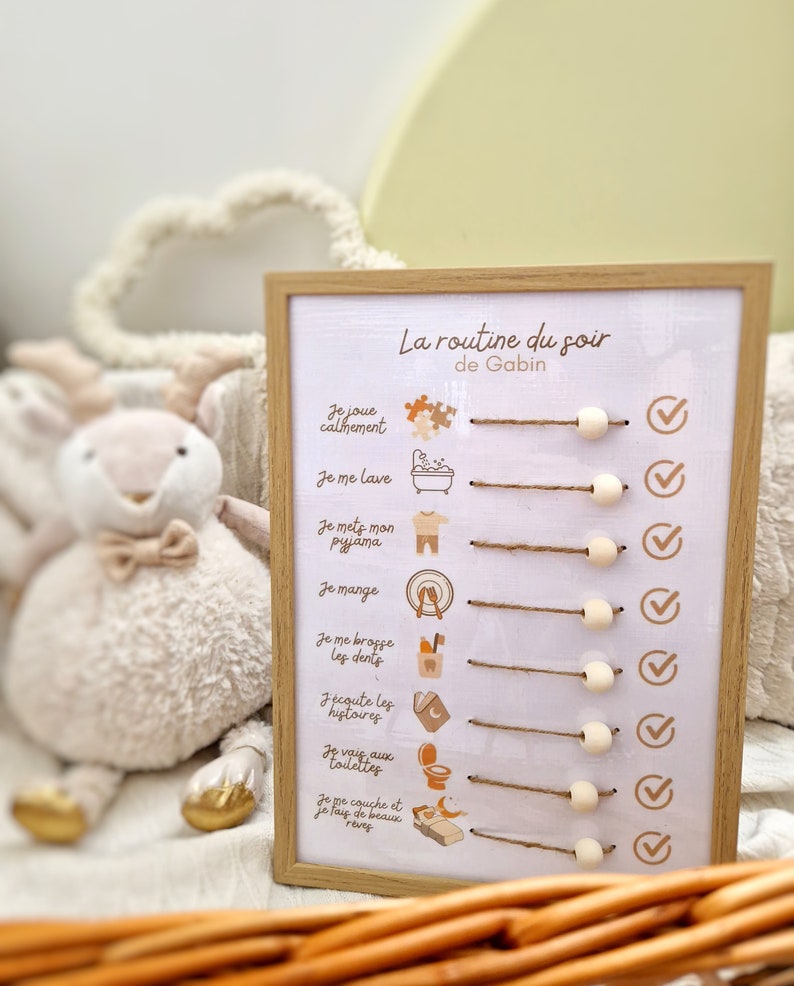 May include: A framed bedtime routine chart with the text "La routine du soir de Gabin". The chart includes illustrations and check boxes for each activity. A stuffed animal is in the background.