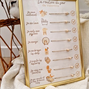 May include: A framed, gold-colored chart titled "La routine du soir de Valentina" with illustrated steps for a bedtime routine. The chart includes text and icons for activities like playing, bathing, and sleeping. The frame is rectangular.