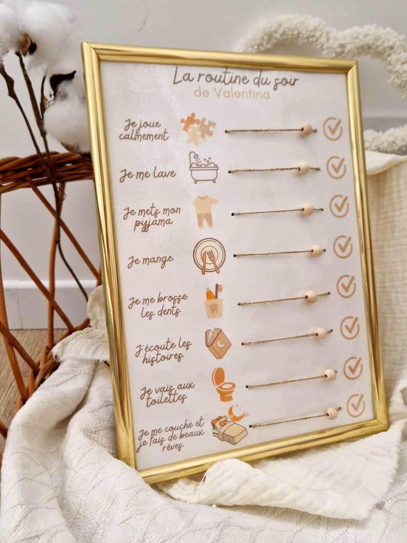 May include: A framed, gold-colored chart titled "La routine du soir de Valentina" with illustrated steps for a bedtime routine. The chart includes text and icons for activities like playing, bathing, and sleeping. The frame is rectangular.