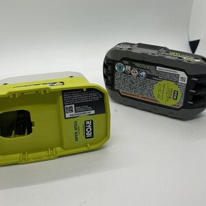 Pu&ograve; includere: Due componenti della batteria per utensili elettrici Ryobi da 18 V. Uno &egrave; una base caricatore verde lime e bianca con il testo "YOUR NAME" e "RYOBI". L'altro &egrave; un pacco batteria nero e grigio con un adesivo verde e varie etichette.