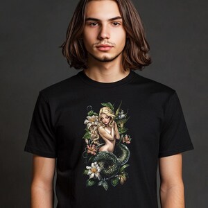 Peut inclure: T-shirt noir avec un imprimé graphique d'une femme aux longs cheveux blonds enroulés autour d'un serpent vert. La femme est entourée de fleurs et de feuilles.