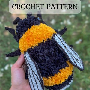 Peut inclure: Un bourdon au crochet fait à la main avec des détails noirs, jaunes et blancs. L'insecte en peluche a de grandes ailes et est étiqueté "CROCHET PATTERN". L'abeille est un article d'artisanat doux et texturé.
