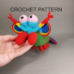 May include: Crochet pattern for a colorful, whimsical creature with large eyes, red claws, and a green body. The creature has a segmented body and a long tail.