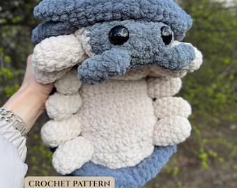 May include: A plush, handmade crochet toy shaped like an isopod, featuring a dark blue top shell and a cream-colored underside with multiple rounded segments. The creature has two large, shiny black plastic eyes and the text CROCHET PATTERN.