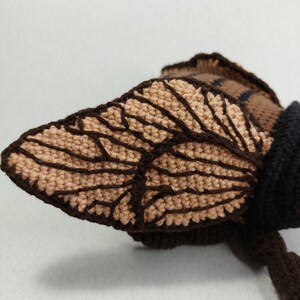 May include: Close-up of a crocheted bee with brown and tan wings. The bee is made with brown, tan, and black yarn.