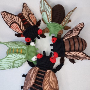 May include: Five crocheted insect toys, each with a different color and pattern. The insects are a cicada, a beetle, a dragonfly, a ladybug, and a moth. The toys are all handmade and have a whimsical, colorful design.