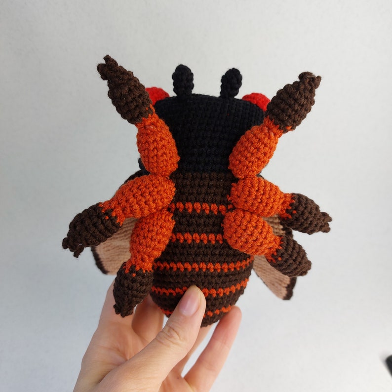 May include: A crocheted bee plush toy with brown and orange stripes. The bee has black eyes and red accents on its head.
