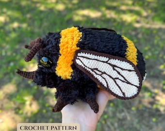 May include: A plush bumblebee toy made of black and yellow fuzzy yarn with large black plastic eyes and two cream-colored crocheted wings featuring dark brown embroidered vein details. The text CROCHET PATTERN is printed in the lower left corner.