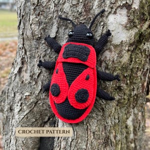 Puede incluir: Un juguete de escarabajo tejido a ganchillo a mano con cuerpo negro, alas de color rojo brillante y puntos circulares negros. El insecto tiene dos antenas, seis patas y dos ojos negros brillantes. El texto CROCHET PATTERN aparece abajo a la izquierda.