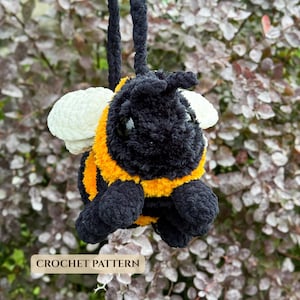 Puede incluir: Un juguete de peluche con forma de abeja hecho con hilo negro y amarillo, con alas blancas y grandes ojos negros. La abeja tiene un lazo de hilo negro para colgar y lleva el texto CROCHET PATTERN en la parte inferior de la imagen.