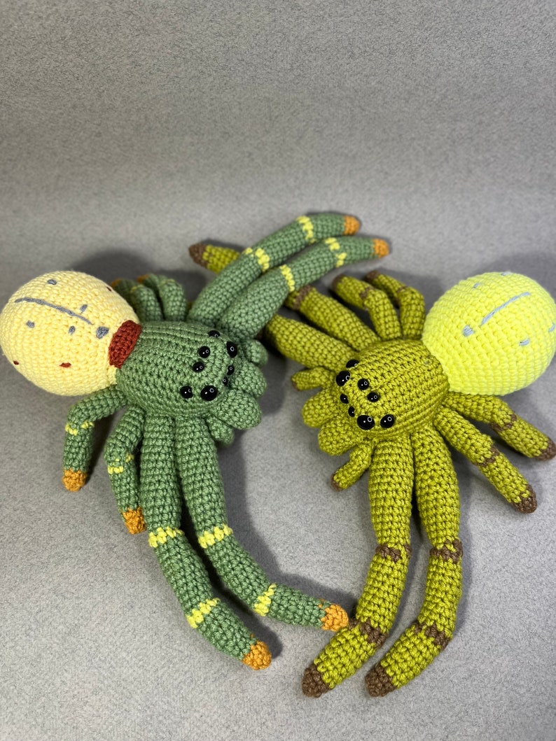 May include: Two crocheted spider plushies, one green with yellow accents and a yellow head with red markings, the other green with yellow accents and a yellow head.