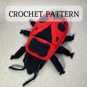 May include: Crochet pattern for a ladybug amigurumi toy. The ladybug is red with black spots and a black head with white eyes. The toy is made with yarn and has a crocheted texture.