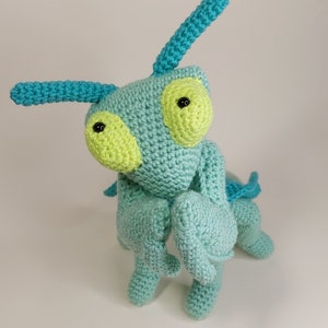 May include: A crocheted green and blue praying mantis toy with black eyes and yellow accents.
