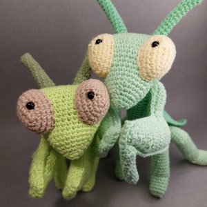 May include: Two crocheted green praying mantis toys. One is larger and has yellow eyes, the other is smaller and has brown eyes.
