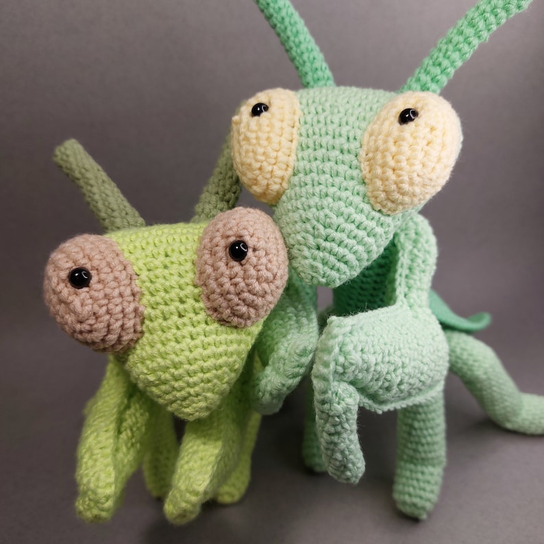 May include: Two crocheted green praying mantis toys. One is larger and has yellow eyes, the other is smaller and has brown eyes.