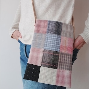 Może przedstawiać: Torba na ramię z patchworku z beżowym paskiem. Torba posiada kwadraty z różowej, szarej, czarnej i niebieskiej tkaniny w kratę. Osoba ma na sobie kremowy sweter i niebieskie dżinsy. Pasek ma około 100 cm długości.