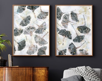 May include: Two framed prints with a white background and a pattern of gray and brown ginkgo leaves. The frames are a light wood color.
