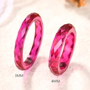 May include: Two vibrant fuchsia pink rings with a faceted, geometric surface texture. The ring on the left is labeled 3MM, and the ring on the right is labeled 4MM, indicating their respective widths. Both rings feature a polished finish.