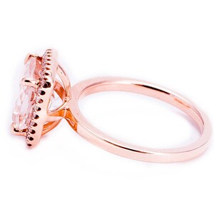 Pu&ograve; includere: Un anello in oro rosa con una grande pietra preziosa quadrata trasparente circondata da un alone di pietre preziose pi&ugrave; piccole.