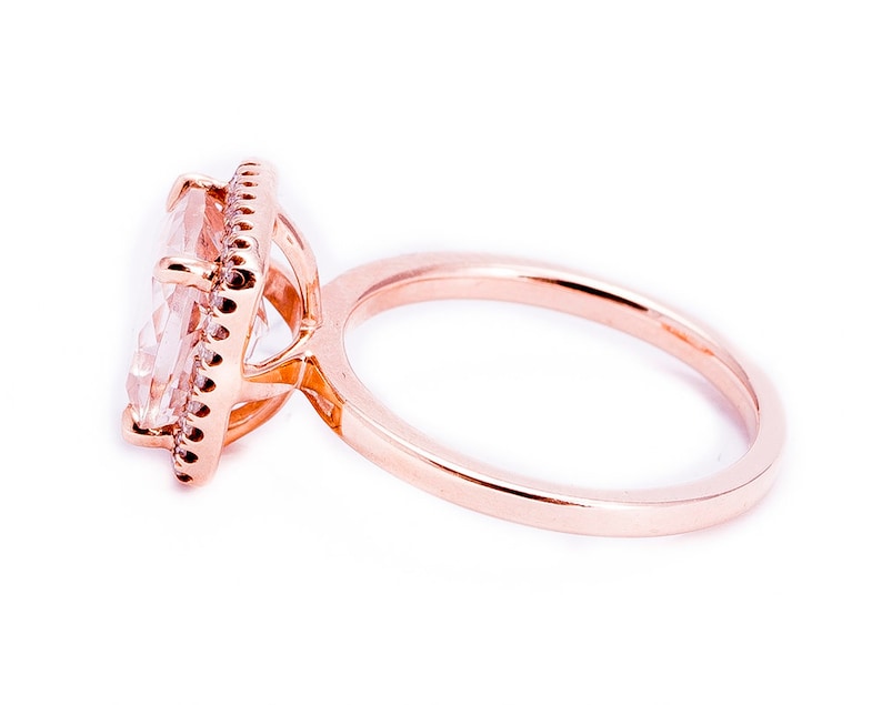Pu&ograve; includere: Un anello in oro rosa con una grande pietra preziosa quadrata trasparente circondata da un alone di pietre preziose pi&ugrave; piccole.