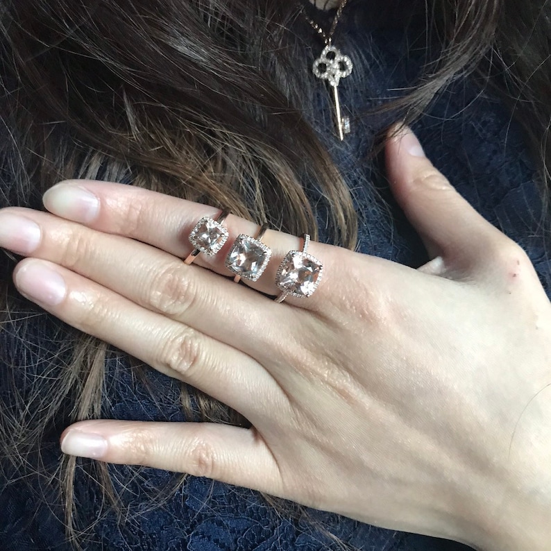 Pu&ograve; includere: Tre anelli in oro rosa con pietre preziose di morganite di forma quadrata e montature a halo di diamanti. Gli anelli sono disposti in ordine di grandezza, con l'anello pi&ugrave; grande a destra.