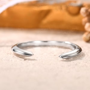 Puede incluir: Un anillo de plata pulida con un diseño abierto único. El anillo tiene una banda lisa y redondeada que se estrecha hacia dos extremos puntiagudos. El anillo está sobre un fondo neutro, resaltando su estilo minimalista.
