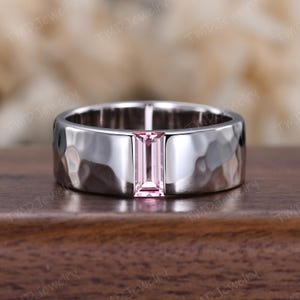 May include: A silver ring with a hammered texture and a rectangular, light pink gemstone. The ring has a wide band and a polished finish, showcasing the gemstone's color.