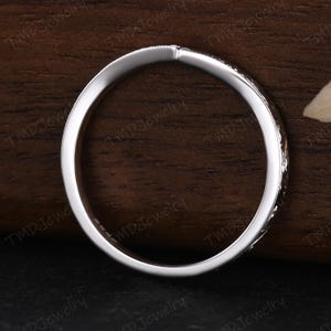 May include: A thin, polished silver-toned metal ring with a smooth inner band and a textured, patterned outer surface. The interior of the band features a small, stamped hallmark indicating its composition, visible against the metallic finish.