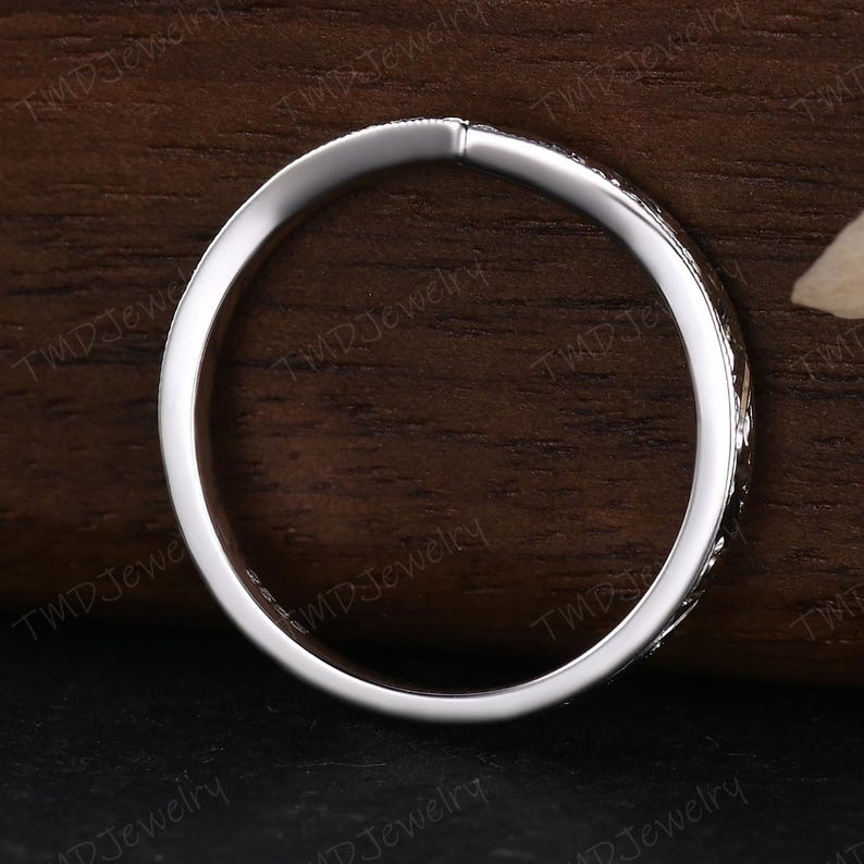 May include: A thin, polished silver-toned metal ring with a smooth inner band and a textured, patterned outer surface. The interior of the band features a small, stamped hallmark indicating its composition, visible against the metallic finish.