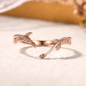 Könnte beinhalten: Ein zarter Ring aus Roségold mit einem Blattdesign und kleinen, klaren Steinen. Der Ring ist an einer Seite offen, was einen einzigartigen und modernen Look erzeugt.