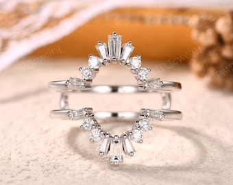 May include: A silver ring guard with a curved design, featuring a series of small, sparkling diamonds and baguette-cut stones. The ring guard is designed to sit alongside another ring, enhancing its appearance.