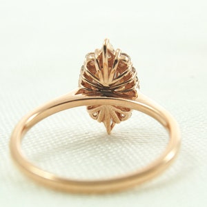 May include: A rose gold ring with a pear-shaped diamond set in a delicate, floral-inspired halo setting. The ring is shown from the back, showcasing the intricate details of the halo.
