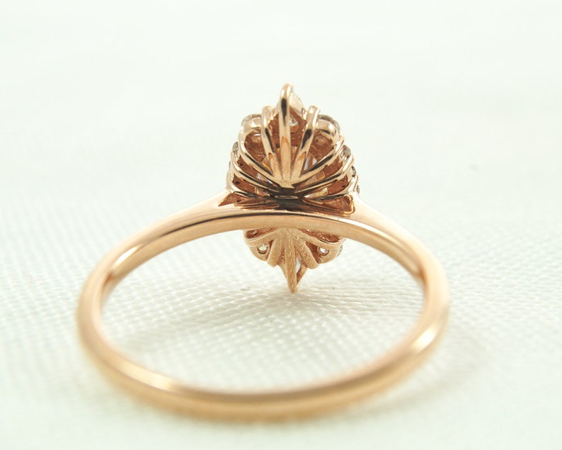 May include: A rose gold ring with a pear-shaped diamond set in a delicate, floral-inspired halo setting. The ring is shown from the back, showcasing the intricate details of the halo.