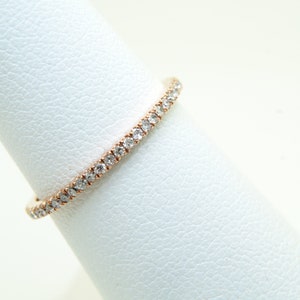 May include: A delicate eternity band ring with a continuous row of small, sparkling diamonds set in a rose gold band.