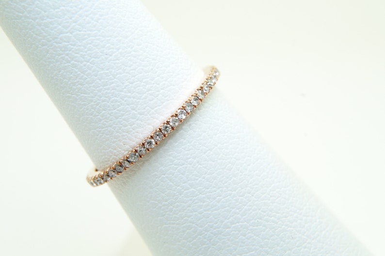 May include: A delicate eternity band ring with a continuous row of small, sparkling diamonds set in a rose gold band.
