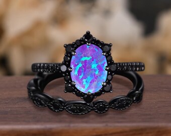 May include: A black ring set featuring an oval-cut, iridescent opal gemstone with purple and blue hues. The main ring is surrounded by black gemstones, and the band is also black. The set includes a matching band.
