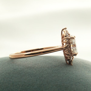 May include: A rose gold engagement ring with a large oval-shaped center stone surrounded by smaller diamonds.