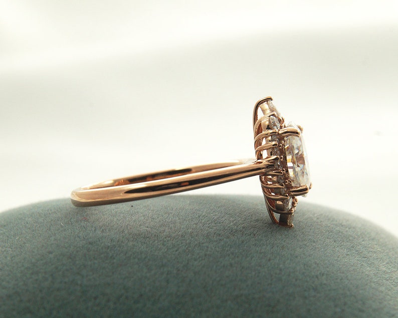 May include: A rose gold engagement ring with a large oval-shaped center stone surrounded by smaller diamonds.