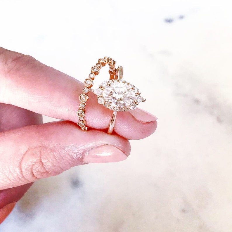 May include: A pear-shaped diamond engagement ring with a halo setting and a delicate band. The ring is paired with a matching diamond eternity band.