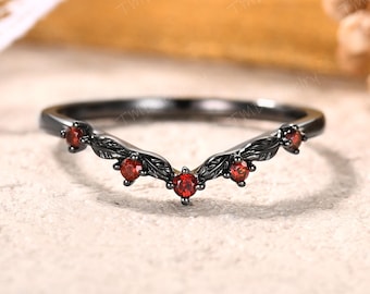 May include: A black metal V-shaped ring featuring a delicate leaf-inspired band design. The ring is set with five small, round, vibrant red gemstones spaced evenly along the curved front, creating a distinct contrast against the dark metal finish.