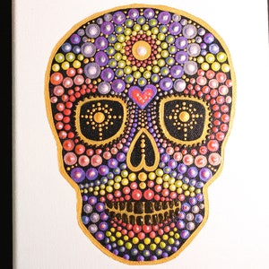 May include: A colorful, hand-painted sugar skull on a white canvas. The skull is made up of small, round dots in shades of pink, purple, yellow, and green. The eyes are black with gold accents, and the nose is a small, red heart.