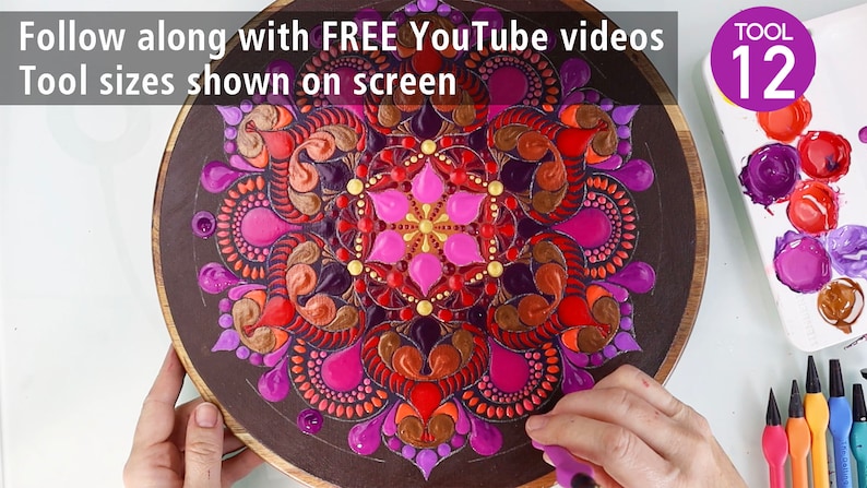 Puede incluir: Primer plano de una tabla redonda de madera con un dise&ntilde;o de mandala colorido pintado sobre ella. El mandala presenta una variedad de colores, incluyendo rosa, rojo, naranja, dorado y morado. El dise&ntilde;o es intrincado y detallado, con una variedad de formas y patrones. La tabla est&aacute; rodeada por una superficie blanca con una paleta de colores de pintura y un conjunto de herramientas para pintar con puntos. El texto "TOOL 12" es visible en la esquina superior derecha de la imagen.